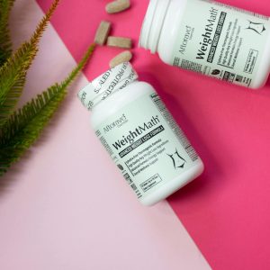 Two weight loss supplement bottles on a vibrant pink surface with scattered pills and greenery.